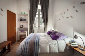 Une chambre à coucher avec un lit, un bureau avec une lampe, une étagère avec des objets et une fenêtre avec des rideaux.