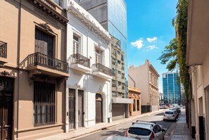 Une rue bordée de bâtiments historiques, un immeuble moderne en verre et des voitures garées.