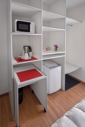 A compact room with a kitchenette, a microwave, a small refrigerator, and a dining area with a red placemat.