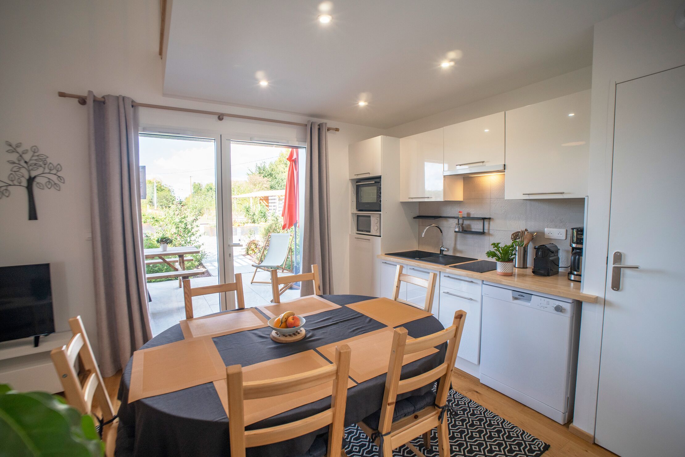 Een moderne keuken met witte kastjes, een vaatwasser en een eethoek met een tafel en stoelen.