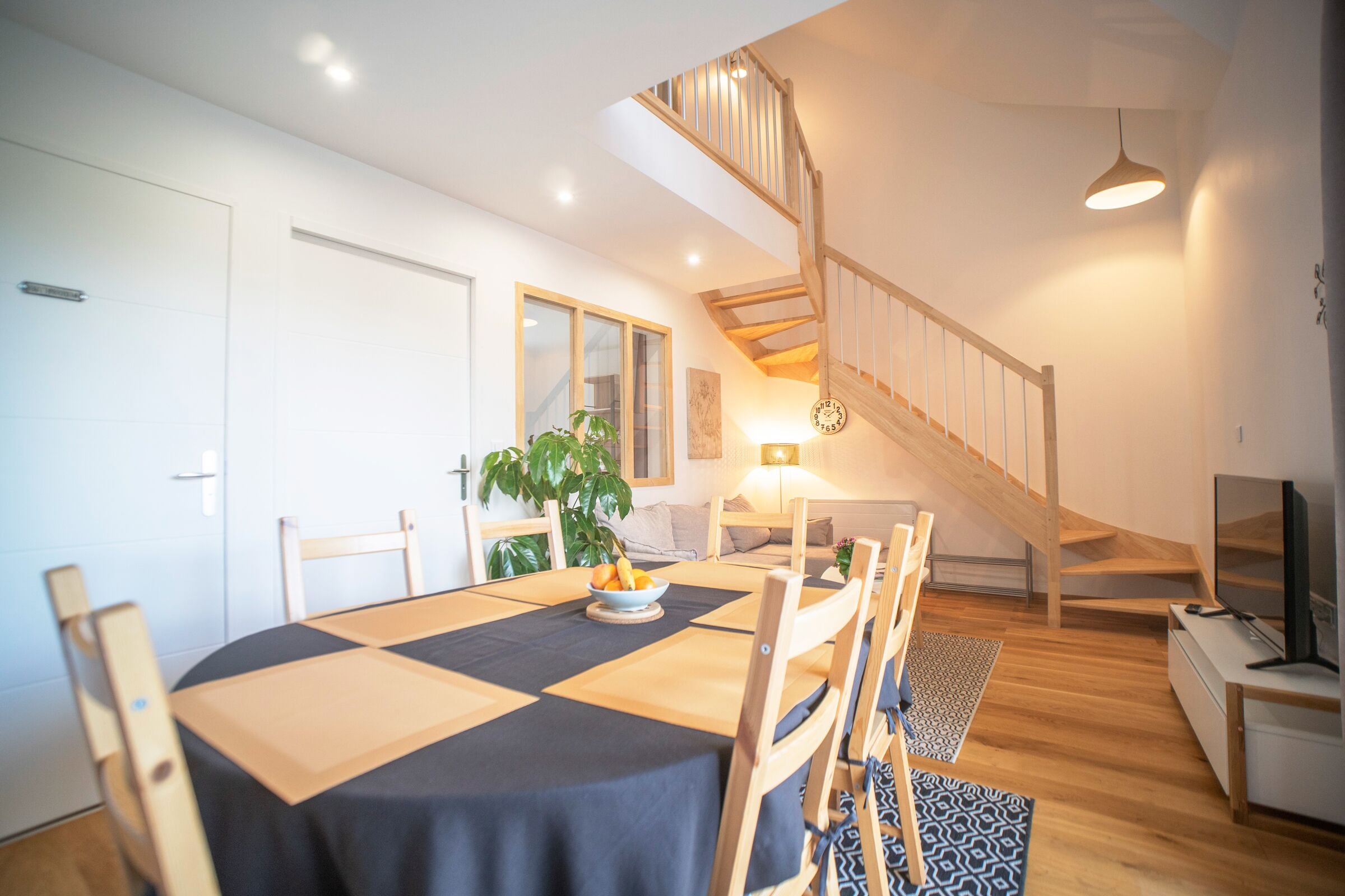 Ein modernes Wohnzimmer mit Essbereich, Treppe und Fernseher.