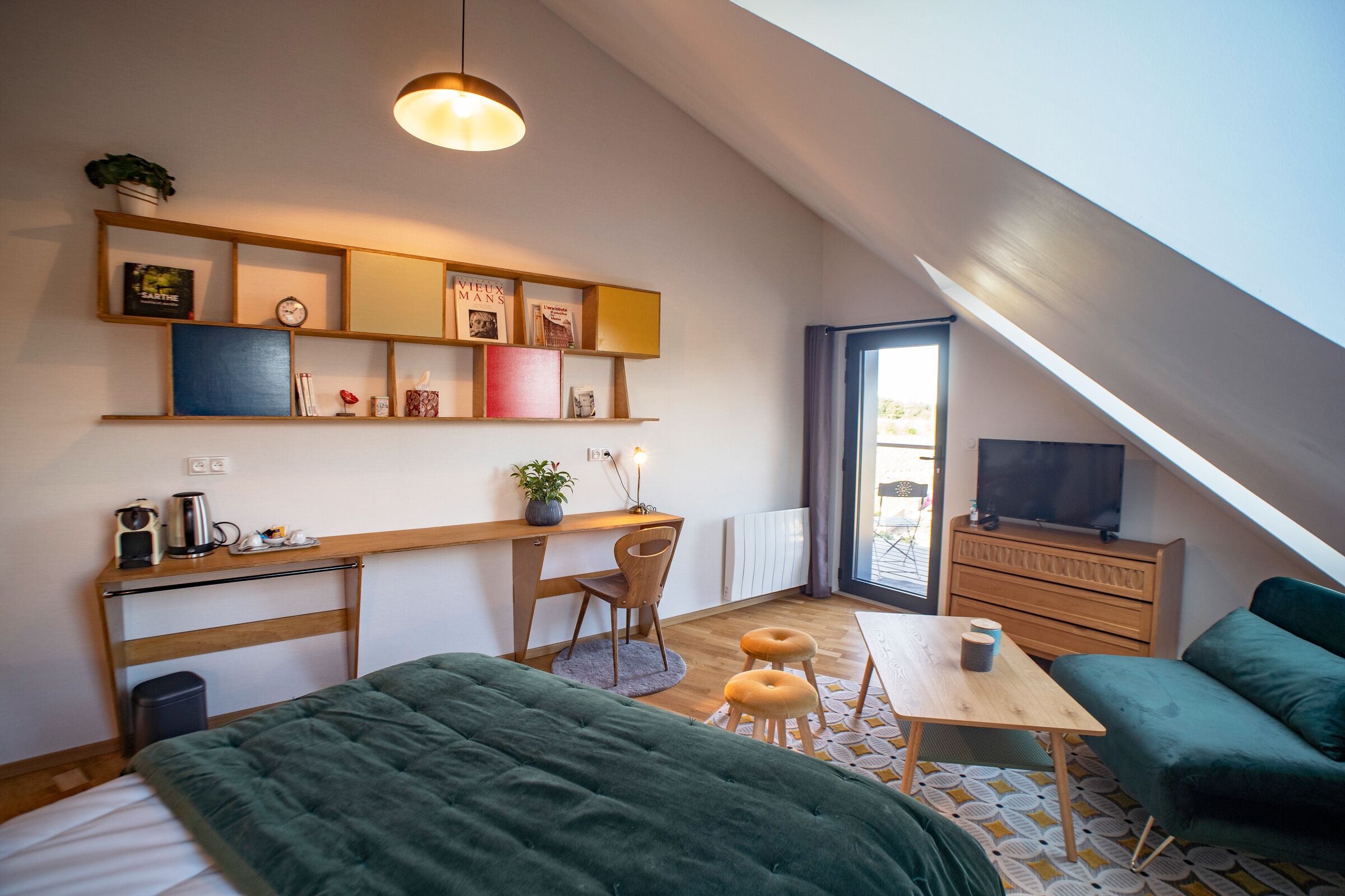 Ein gemütliches Schlafzimmer im Loft-Stil mit schrägem Dach, einem Bett, einem Schreibtisch mit Stuhl, einem Fernseher und einer Couch.