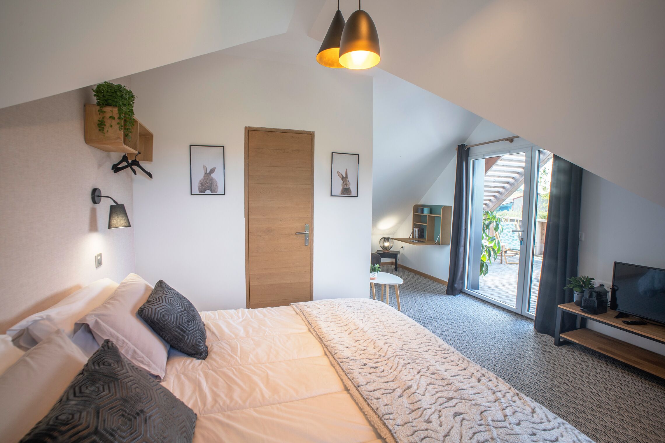 Un dormitorio moderno con una cama grande, una puerta de madera, una mesita pequeña, un televisor y vistas al exterior.