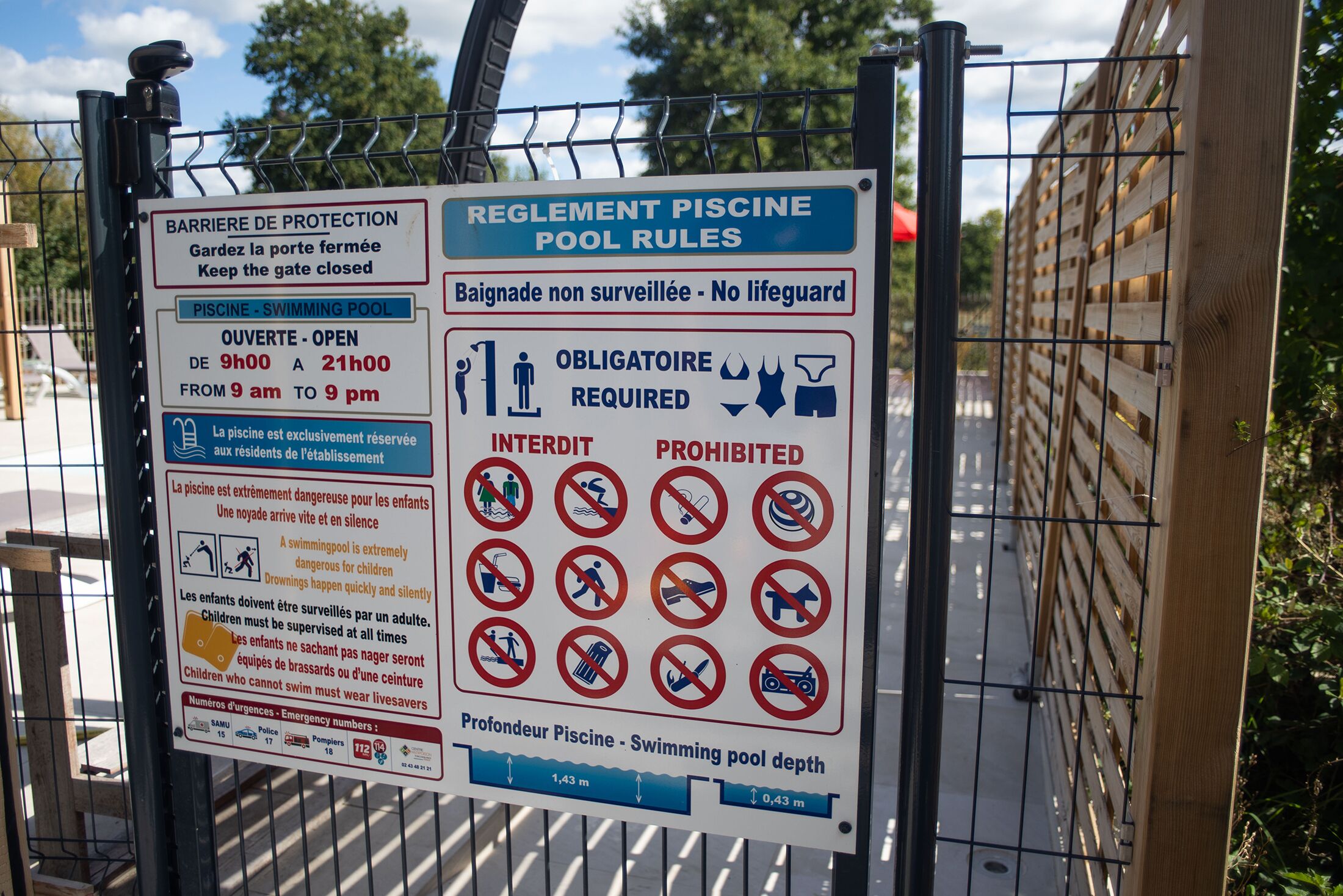 A sign with pool rules and emergency numbers.