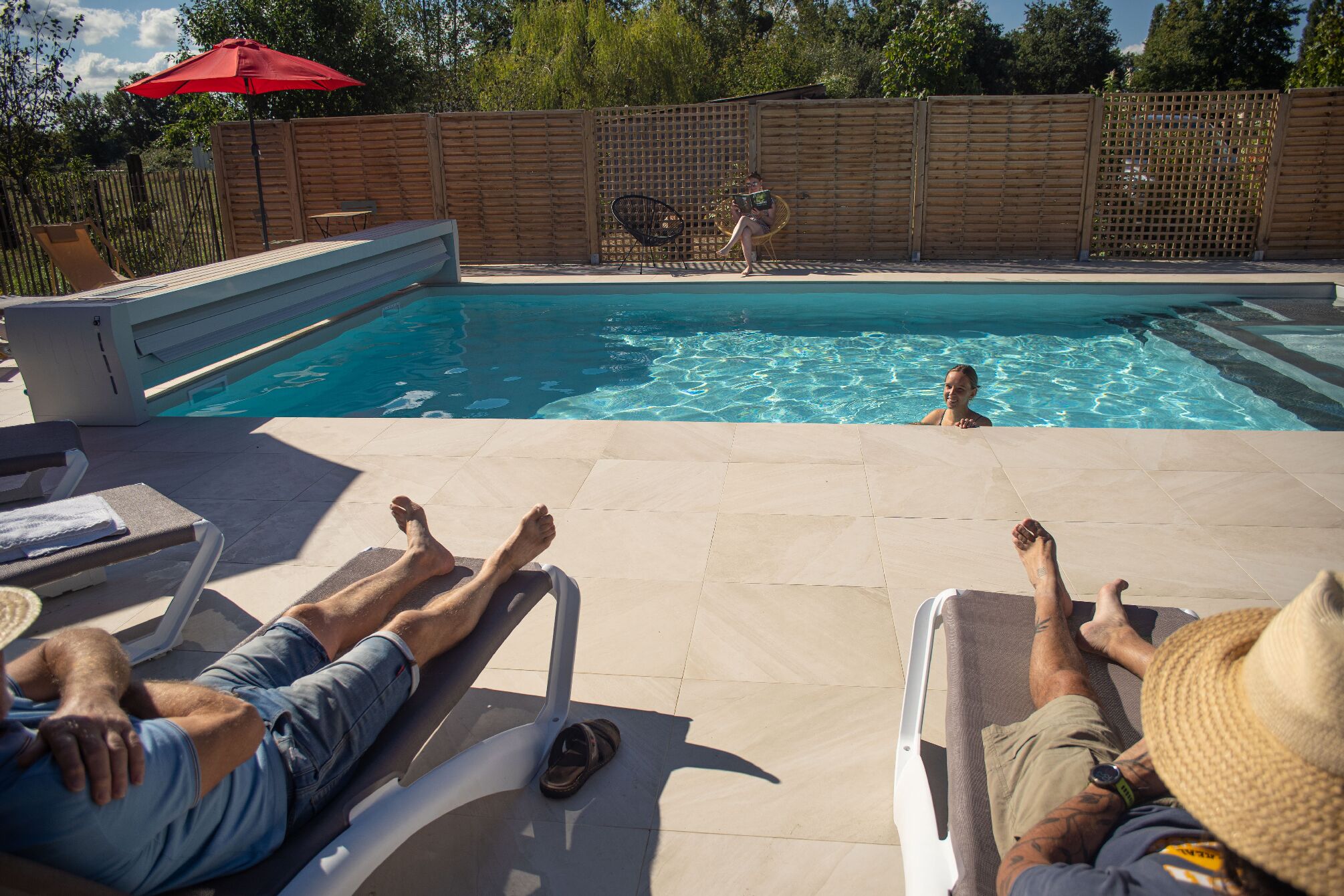 Zona de piscina con sillas de descanso, valla de madera y sombrilla roja.