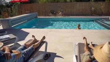Zona de piscina con sillas de descanso, valla de madera y sombrilla roja.