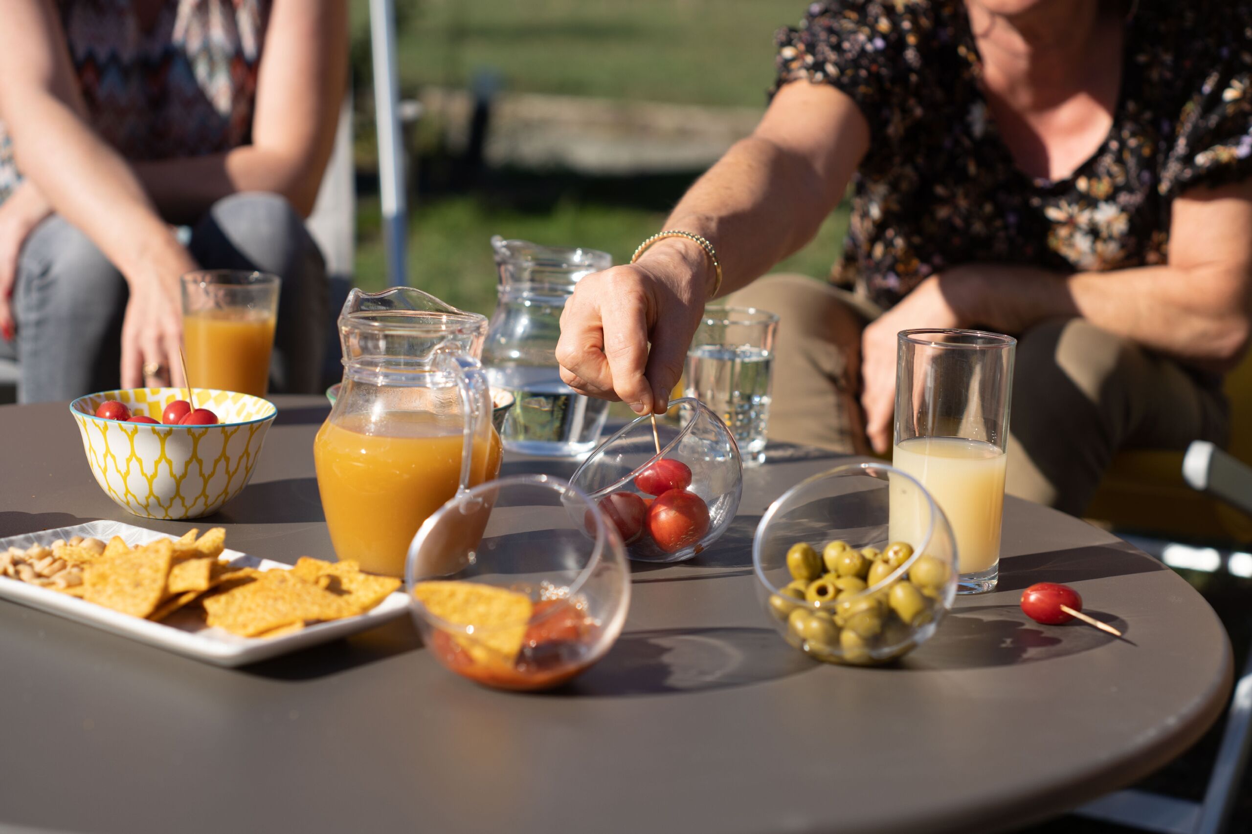 Une table est dressée avec divers aliments et boissons, notamment une carafe de jus d’orange, des bols de cerises et d’olives, et une assiette de chips.