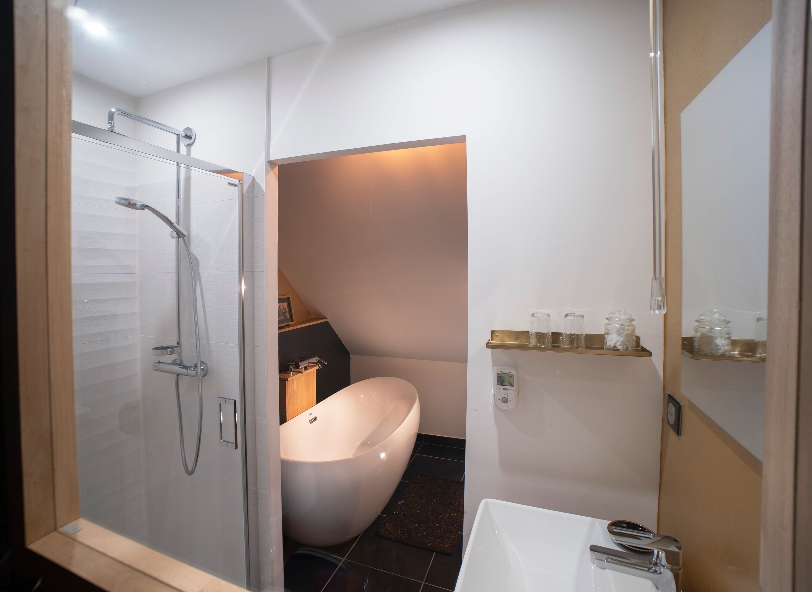 Een moderne badkamer met een douche in een glazen cabine, een vrijstaand bad en een witte wastafel.