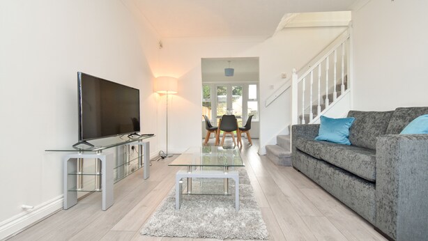 A modern living room with a flat-screen TV, a glass coffee table, a grey sofa with blue cushions, and a staircase leading to another level. - Kents Hill House (Milton Keynes)