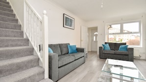 A living room with two grey sofas, a glass coffee table, and a staircase. - Kents Hill House (Milton Keynes)