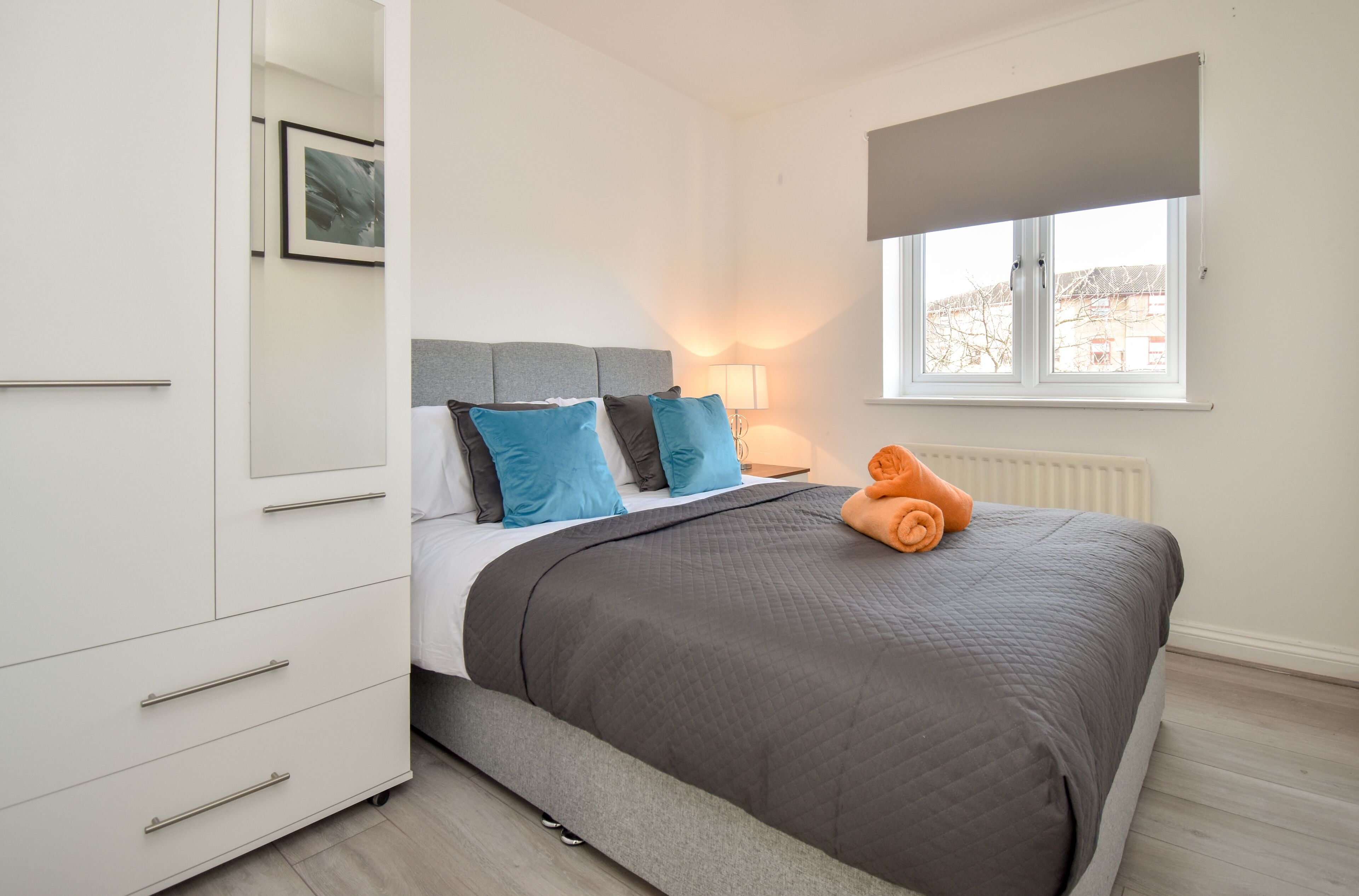 A bedroom with a bed, a nightstand, a lamp, a window with a view, and a wardrobe.