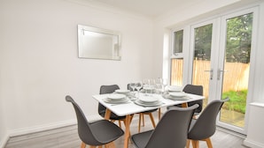 A dining area with a white table set for four, black chairs, and a large mirror on the wall. - Kents Hill House (Milton Keynes)