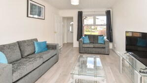 A living room with two grey sofas, a glass coffee table, a flat-screen TV, and a door leading to another room. - Kents Hill House (Milton Keynes)