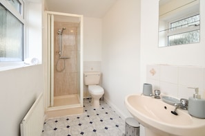 Un baño con ducha, inodoro, lavamanos y ventana.