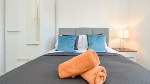 A neatly made bed with a grey quilt, two blue pillows, and an orange towel. - Kents Hill House (Milton Keynes)
