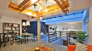 A spacious living area with a high ceiling, wooden beams, a large window, and a balcony with plants. - The Salty Lodge (Lagos)