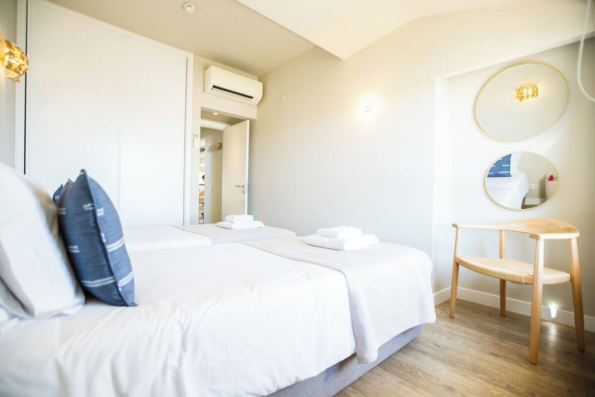 A bedroom with a bed, a chair, a mirror, and an air conditioning unit.