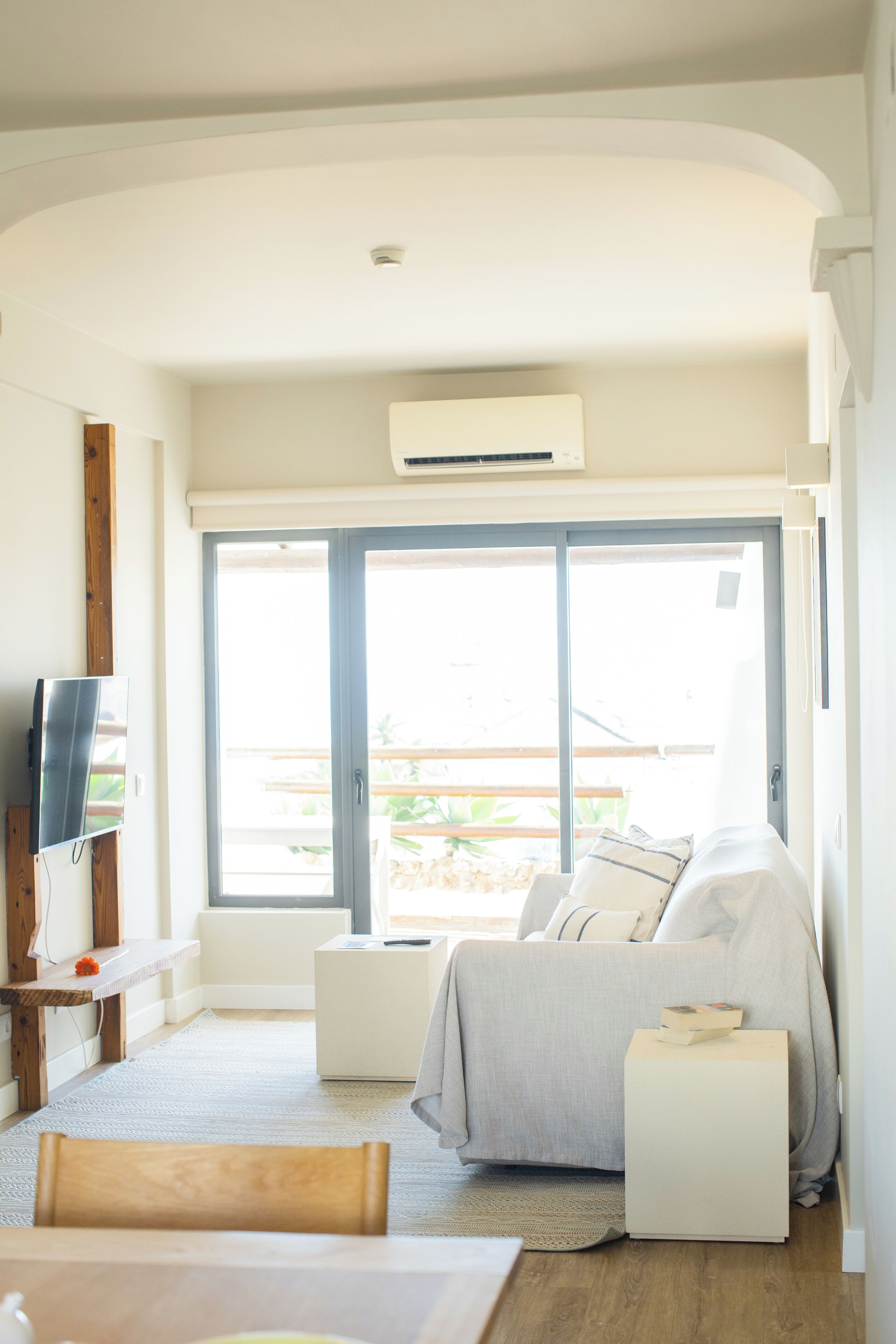 Un dormitorio moderno con cama, mesitas de noche, televisor y un amplio ventanal corredera que da a un área exterior.