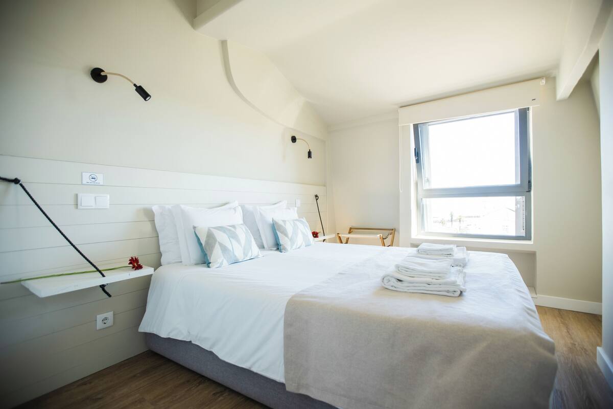 A bedroom with a bed, a window, and a wall-mounted shelf.