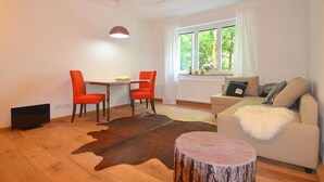 A modern living room with a wooden floor, a sofa, a coffee table, and two red chairs. - Wohnen am Ringpark (Würzburg)