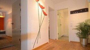 A modern interior with a wooden floor, a wall-mounted poppy decoration, a potted plant, and a visible bathroom door. - Wohnen am Ringpark (Würzburg)
