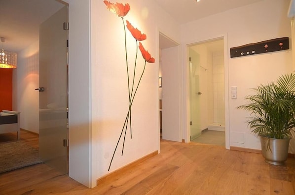 A modern interior with a wooden floor, a wall-mounted poppy decoration, a potted plant, and a visible bathroom door. - Wohnen am Ringpark (Würzburg)