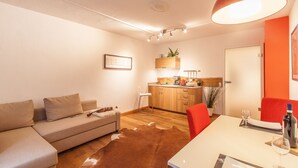 A modern living room with a sofa, a dining table with chairs, a kitchen area, and a ceiling light fixture. - Wohnen am Ringpark (Würzburg)