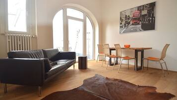 Ein modernes Wohnzimmer mit einer Ledersofa, einem Esstisch mit Stühlen, einem großen Fenster und einem Stadtbildgemälde.