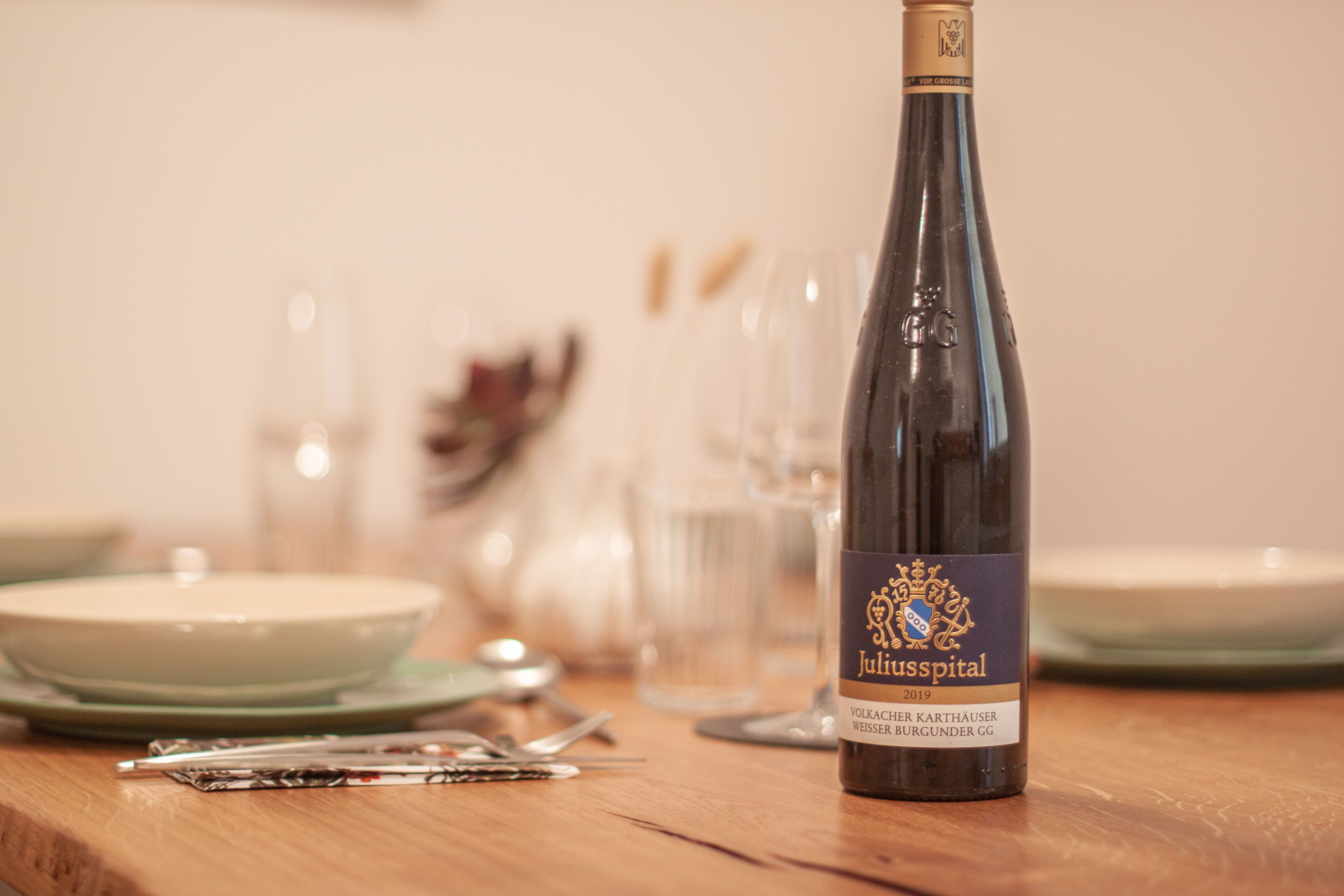 A bottle of Juliusspital wine on a wooden table with plates and cutlery.