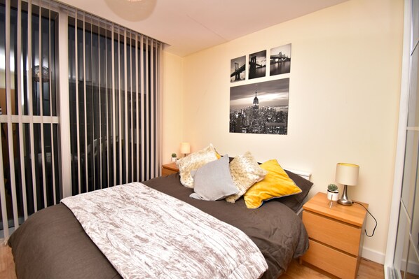 A bedroom with a bed, a nightstand, a lamp, and a cityscape artwork on the wall.
