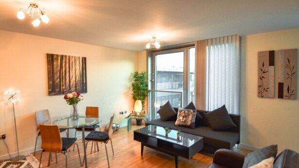 A modern living room with a sofa, coffee table, and chairs. There is a dining table with chairs and a plant. The room has large windows with curtains. - The Hub - Milton Keynes - Instagram Heaven (Milton Keynes)
