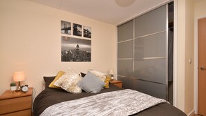 A bedroom with a bed, a nightstand with a lamp, a wall-mounted picture, and a sliding door closet. - The Hub - Milton Keynes - Instagram Heaven (Milton Keynes)