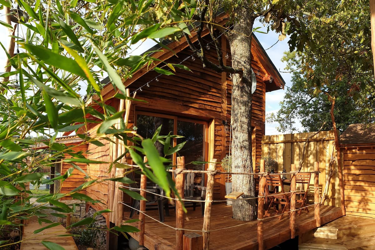 Uma casa na árvore de madeira com varanda, rodeada por bambu e árvores.