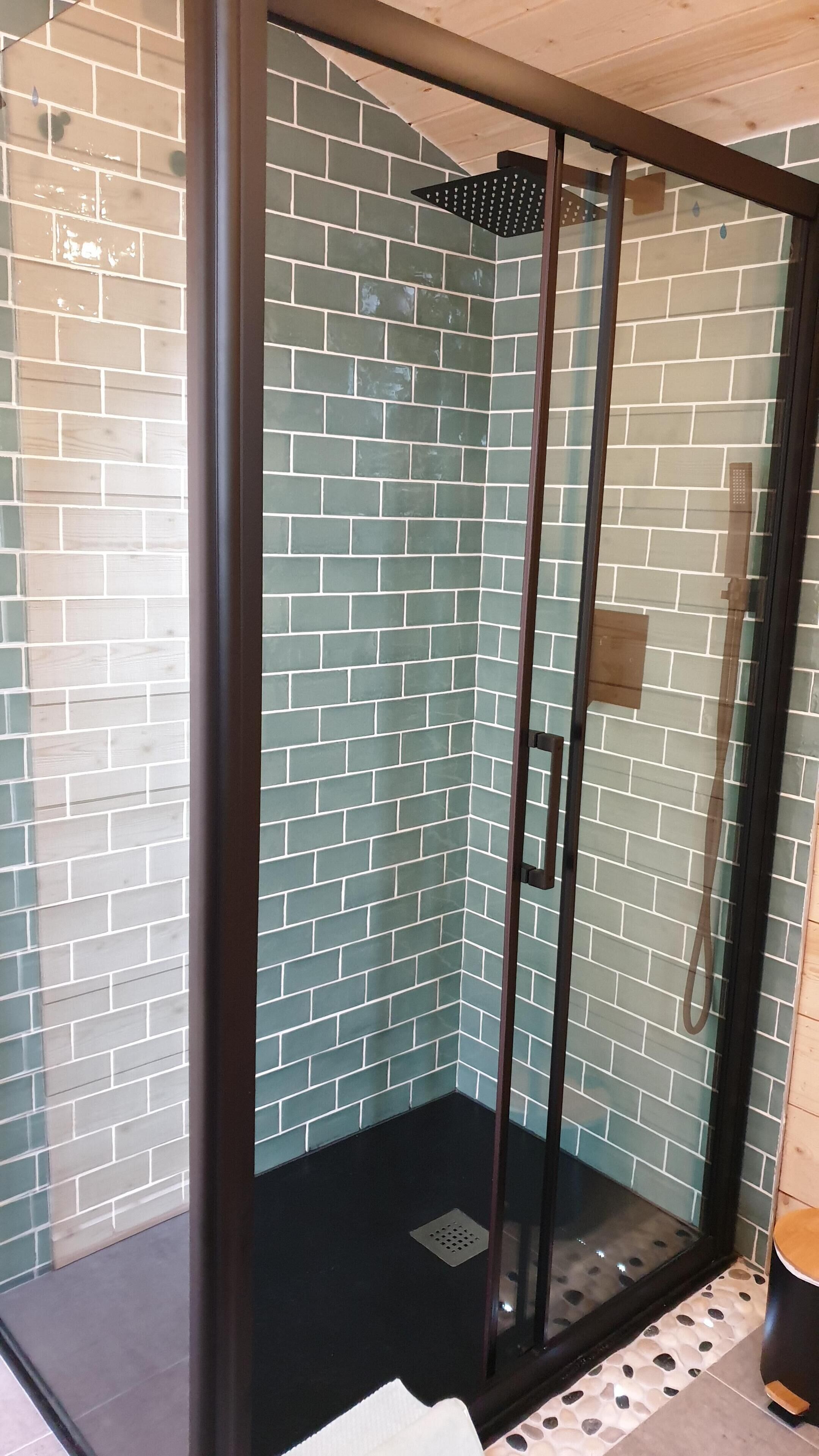 Una ducha con cerramiento de vidrio, pared de azulejos y techo de madera.