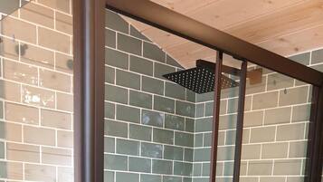 Una ducha con cerramiento de vidrio, pared de azulejos y techo de madera.