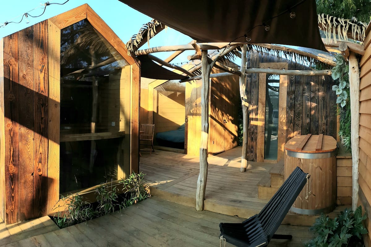 Uma cabana de madeira com varanda, banheira de hidromassagem e uma cadeira.