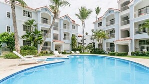Ein Poolbereich mit Liegestühlen und einem kühlen, blauen Pool, umgeben von mehrstöckigen Gebäuden mit Balkonen.