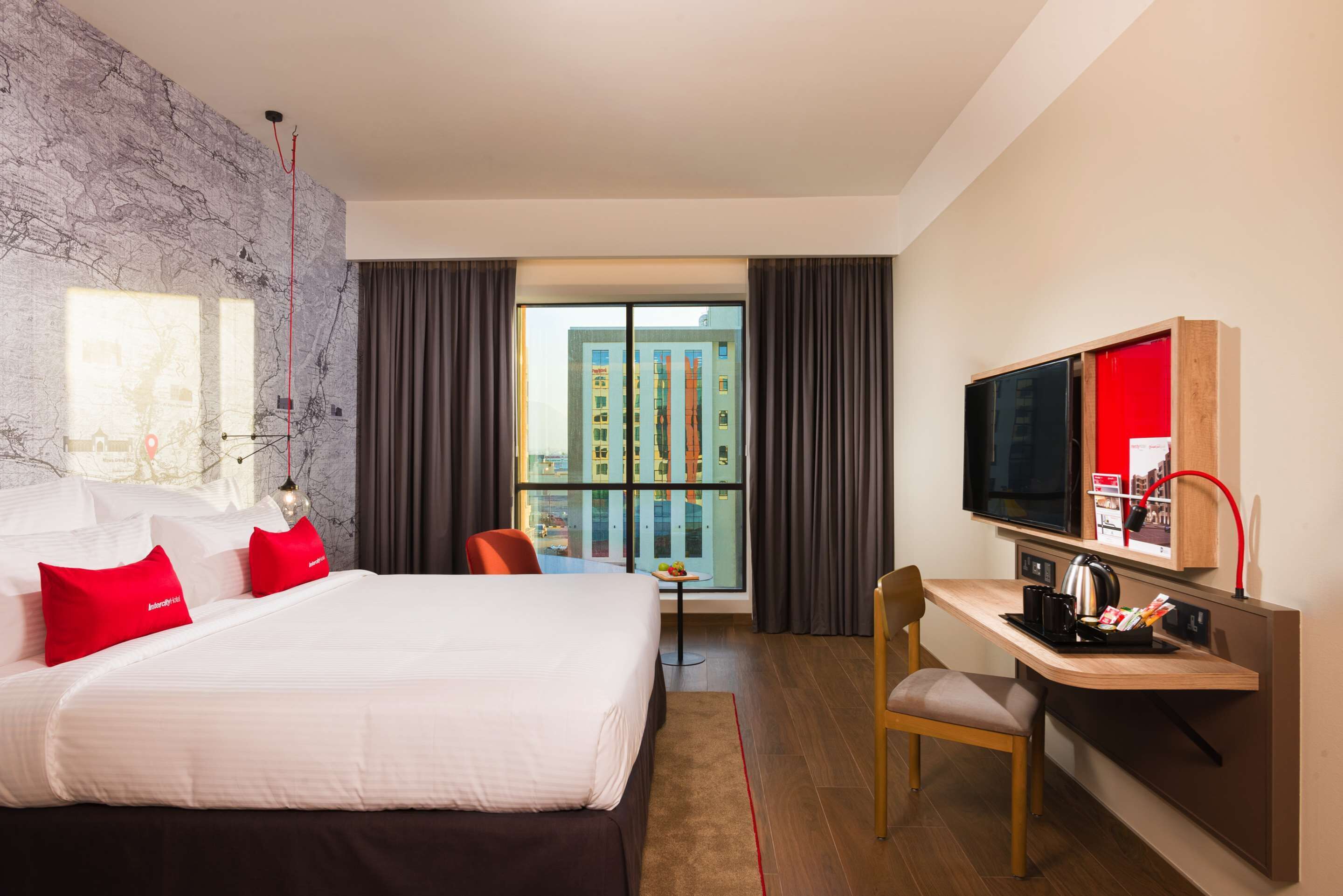 A hotel room with a large bed, a desk with a chair, a television, and a view of a building through the window.