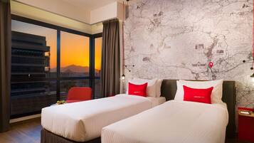 Habitación de hotel con dos camas, un ventanal con vistas a la ciudad, un mapa en la pared y una silla roja.