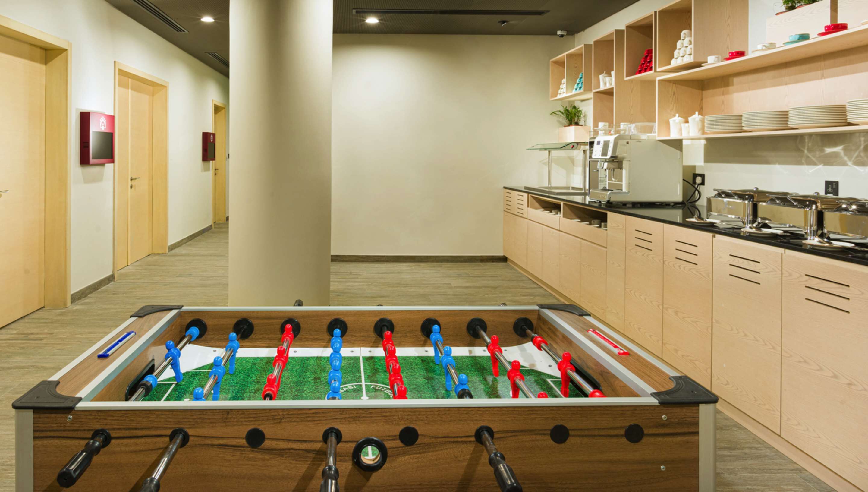 A room with a foosball table, wooden cabinets, and a kitchenette area.