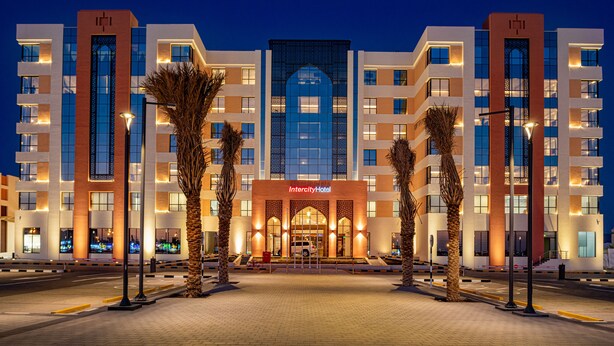 Un hotel moderno con una entrada central, varios pisos y un llamativo fachada de vidrio.