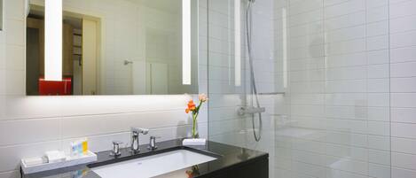 Un baño moderno con un lavabo negro, azulejos blancos, un espejo grande y una ducha con mampara de vidrio.