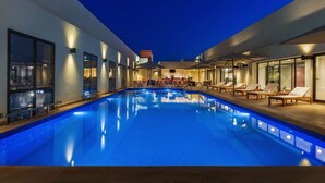 Una piscina con sillas de descanso y tumbonas, rodeada de paredes de vidrio e iluminada con luz ambiental.