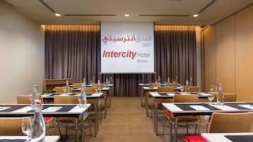 Uma sala de conferências no Intercity Hotel em Nizwa, com mesas preparadas para reuniões, uma tela de projetor e cortinas.