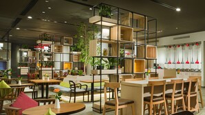 Un interior de restaurante moderno con mobiliario de madera, varias zonas de estar y plantas decorativas.
