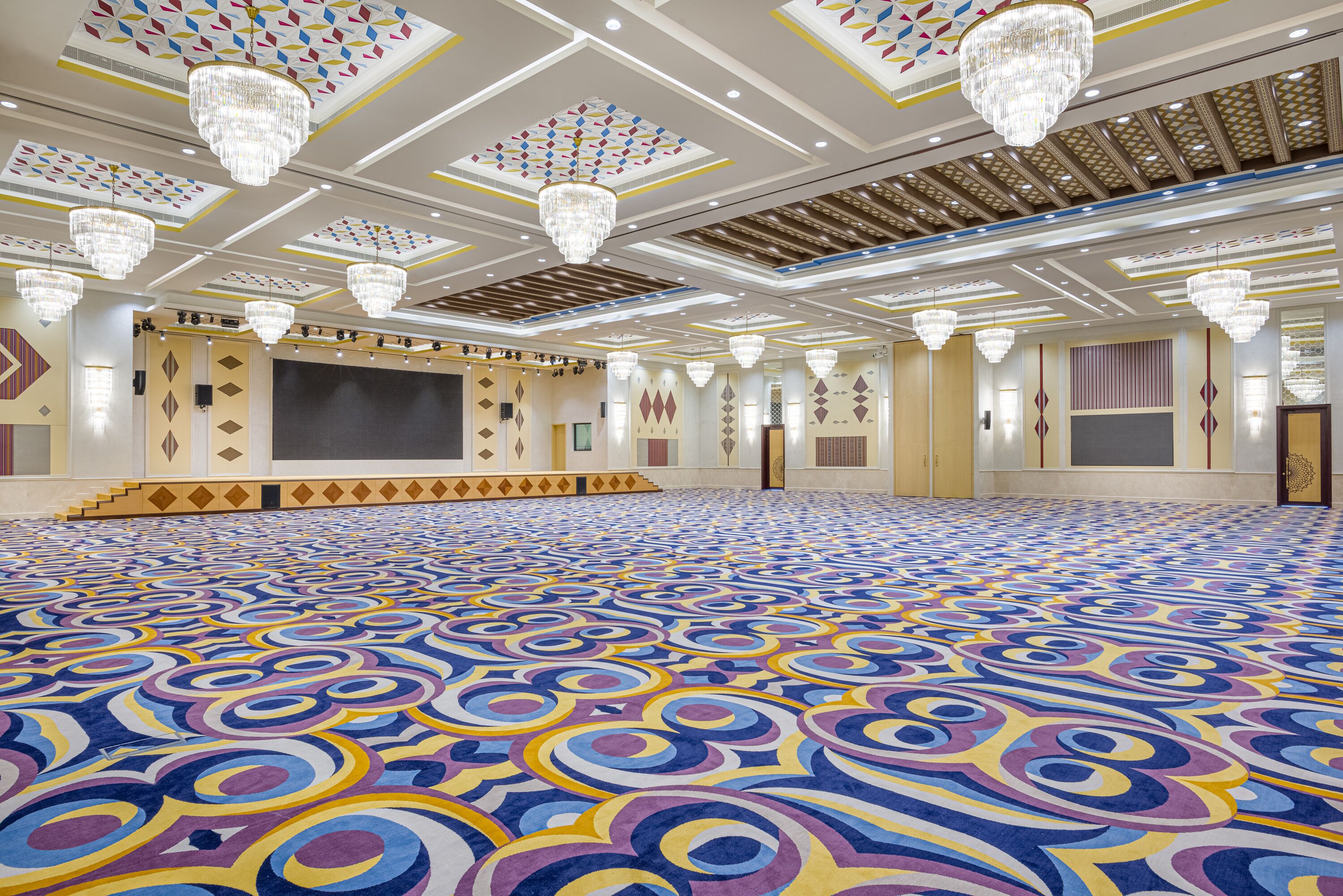 Un amplio salón con alfombra estampada, candelabros y una pantalla grande.