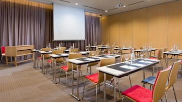 Una sala de conferencias con varias mesas y sillas, una pantalla de proyector y un atril.