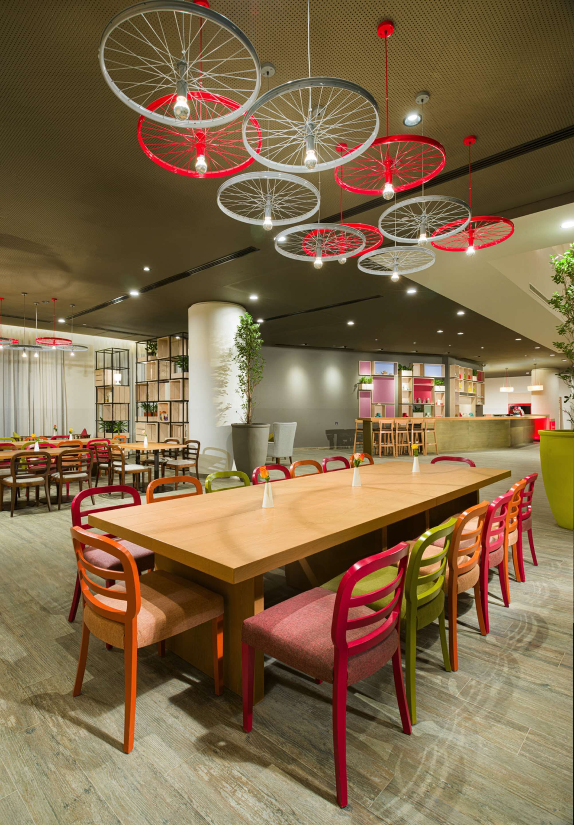 A modern dining area with a long wooden table, colorful chairs, and unique red and white bicycle-themed pendant lights.