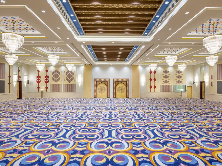 A large conference room with a patterned carpet, chandeliers, and ornate ceiling design.