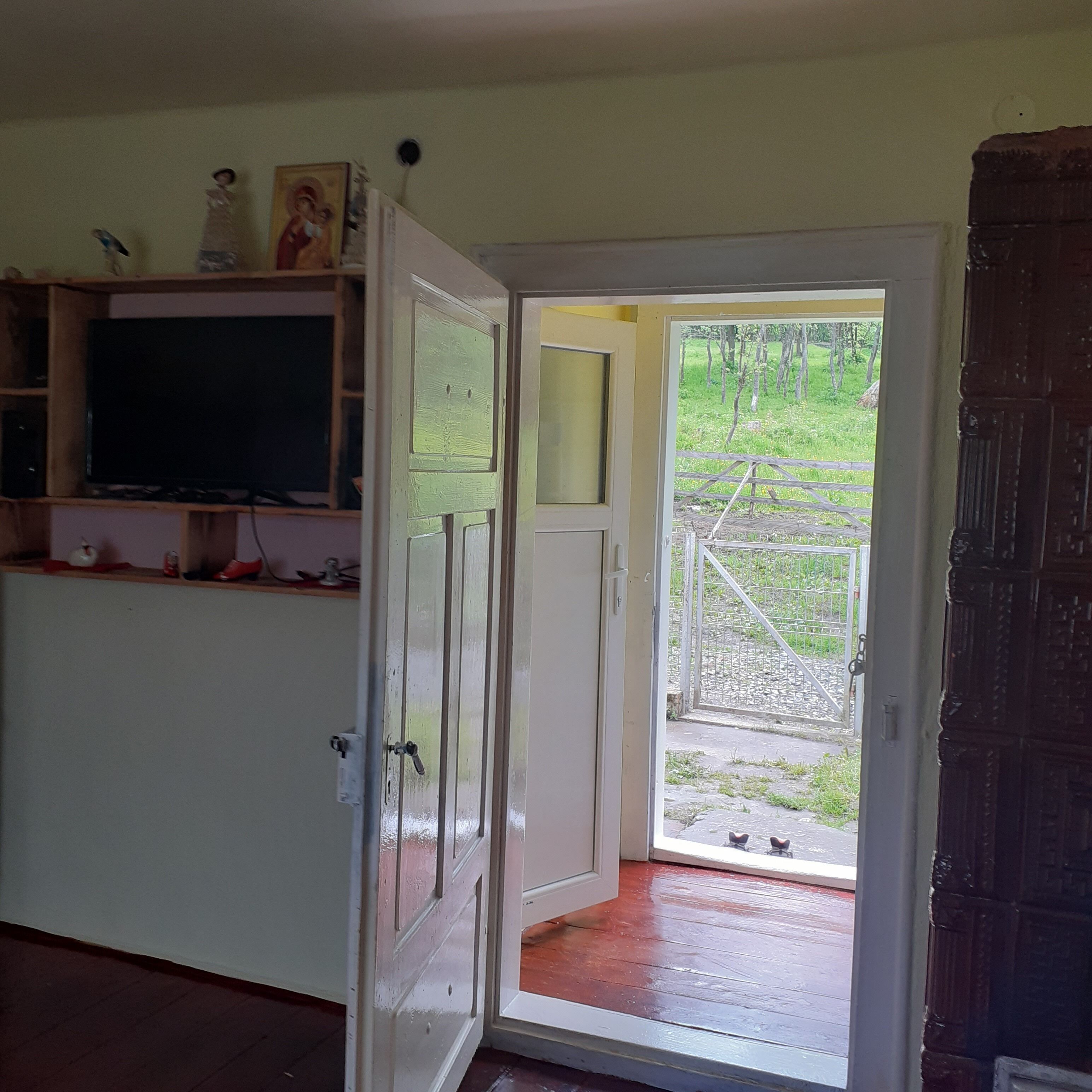 Una habitación con una televisión sobre una estantería, una puerta que da al exterior y un pequeño espacio al aire libre con una verja.